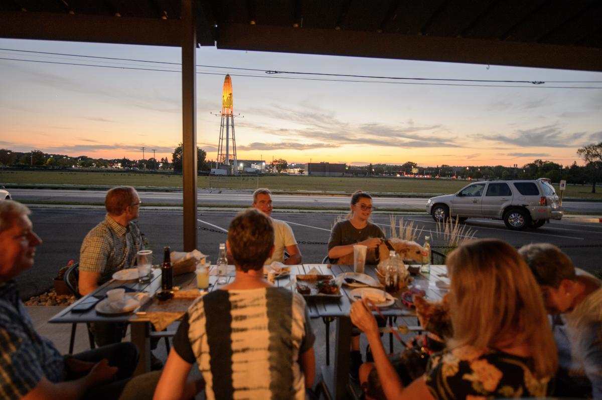 A group eats on the patio of The Workshop Food Hall and Bar with the ear of corn water tower in the background